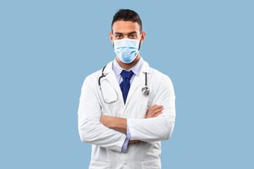 Middle Eastern Male Doctor Wearing Protective Face Mask Over Blue Background