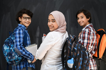 Arabic teenagers, students group portrait against black chalkboard wearing backpack and books in school.Selective focus 