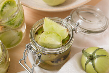 Green tomatoes for canning in a glass jar on a light wooden background. Unripe tomatoes for harvest.