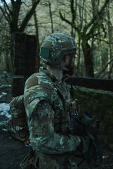 Fototapeta premium Portrait of airsoft player in professional equipment with machine gun in the forest. Soldier with weapons at war