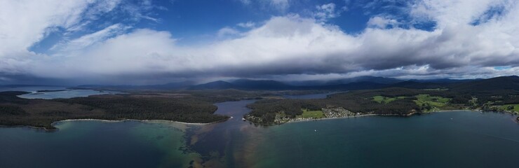 Drone flying over a beach town in tasmania, over the beach and ocean, looking at the clouds and...