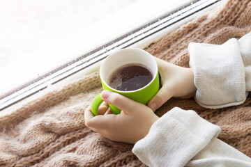 Green cup in children's hands by the window