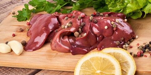 Raw chicken liver on a wooden board, beautifully served with pepper, lemon and herbs