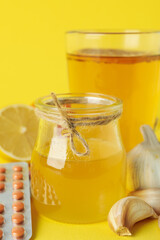 Concept of treatment colds with honey and garlic on yellow background