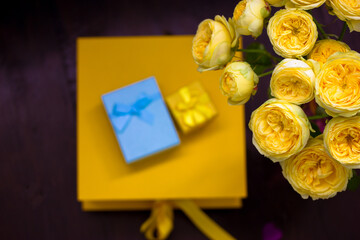 Yellow and blue gift boxes, bouquet of beautiful yellow roses Austin on a dark wooden background view from above. Holiday greeting card for birthday, Mother's Day, anniversary, March 8. Shopping sales