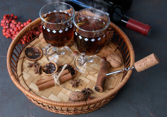 mulled wine in glasses with cardamom stars, cinnamon sticks, rowan berries in a wicker basket on a wooden table, a bottle of wine corkscrew with a cork