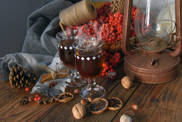 mulled wine in glasses with cardamom stars, cinnamon sticks, rowan berries in a wicker basket on a wooden table, a warm scarf and an old kerosene lamp