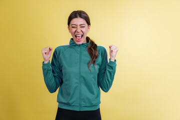 One young emotional girl in green tracksuit standing and shouting isolated on yellow studio background in neon light. Emotions, facial expression