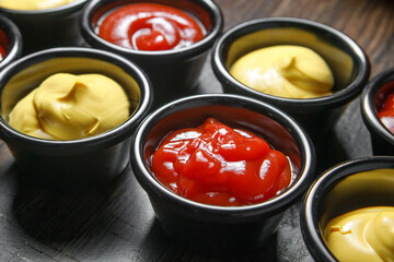 Small cups with ketchup and mustard stand in a row on the table.