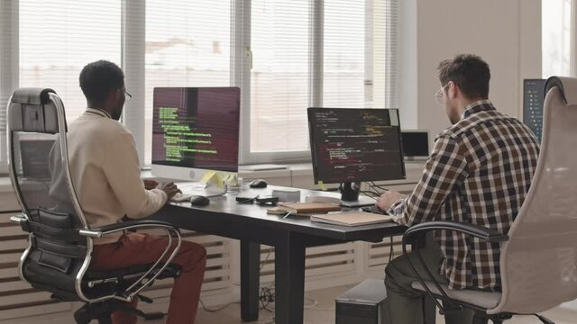 Rear-view slowmo stab shot of two male software developers or engineers writing program codes on pc computers in contemporary office