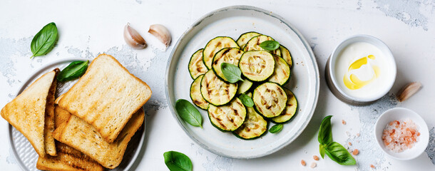 Grilled zucchini salad with basil leaves, yogurt sauce and fried bread in a simple ceramic plate on...