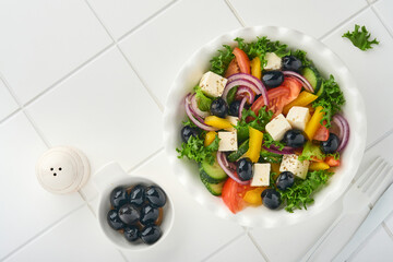 Traditional Greek salad of fresh cucumber, tomato, sweet pepper, lettuce, red onion, feta cheese and olives with olive oil on white plate. Healthy food, top view.