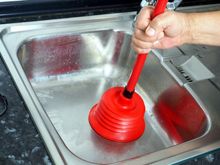 A man cleans a clogged kitchen sink with a red plunger