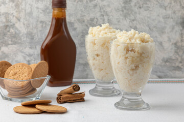 two glasses of rice pudding with cookies, caramel and cinnamon on a table with white tablecloth
