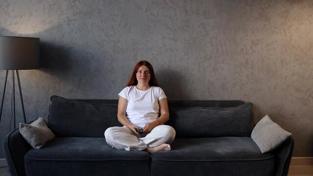 Happy woman relaxing watching television or movie while choosing channel at home living room. Using a remote control