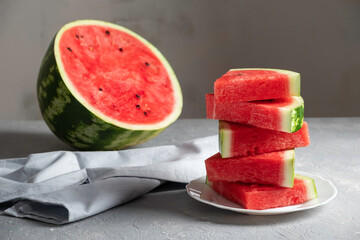 Sliced and half a ripe watermelon on a plate on a gray background. Horizontal orientation, no people, copy space.