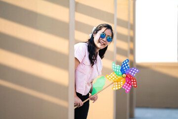 Asian woman posts and play Windmill Toy colourful rainbow colour on the building rooftop in sunset time.