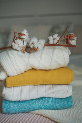 Stack of knitted warm sweaters in wicker rattan basket, plaid, branch of cotton. Autumn mood.
