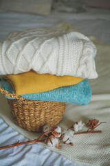 Fototapeta na wymiar Stack of knitted warm sweaters in wicker rattan basket, plaid, branch of cotton. Autumn mood.