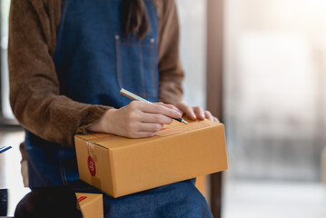 Online sales business owner woman is taking note of the customer's address on the parcel box being prepared for delivery. - obrazy, fototapety, plakaty