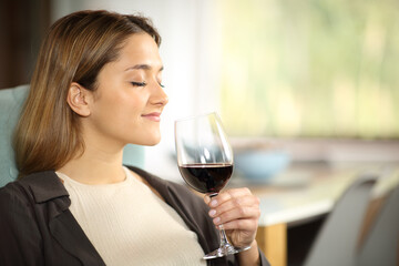 Happy woman smelling red wine at home