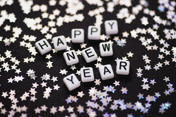 Happy New Year Inscription in silver confetti in the form of stars on black background . Festive day backdrop.