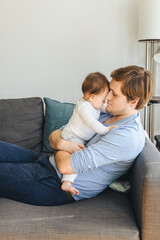 Young Father Carrying Infant Daughter On Sofa
