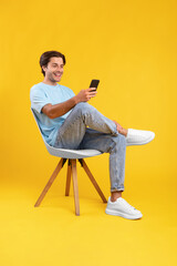 Happy guy using cell phone at studio, sitting on chair