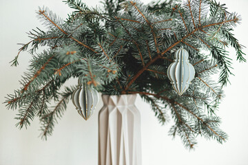 Stylish christmas ornament on fir branch in modern vase close up. Festive simple scandi decor