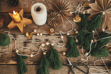 Christmas fir trees garland, bells, stars, candle, thread, scissors on rustic wood. Flat lay