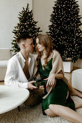 Obraz premium Beautiful young couple exchanging Christmas gifts at home in a bright living room.