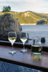 two glasses of white wine and carafe on table with sea and cliffs in the background