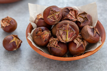 Full Bowl of roasted chestnuts in a shell. Close-up, selective focus, gray concrete background. Healthy snack