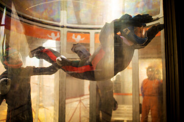 The flight of a young woman in blue helmet in a wind tunnel. Skydiving training. - obrazy, fototapety, plakaty