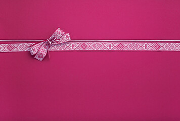 Latvian flag colored (red and white ribbon and bow witth national ornaments on red background.