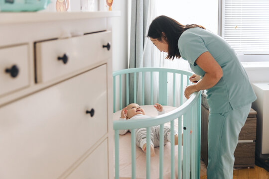 Female nurse looking in on daughter's crib At Home