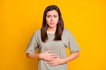 Portrait of pretty sick brown-haired girl touching abdomen feeling bad isolated over bright yellow...