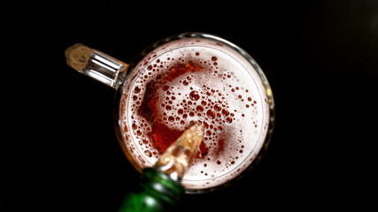 Pouring beer into glass, top shot, black background.