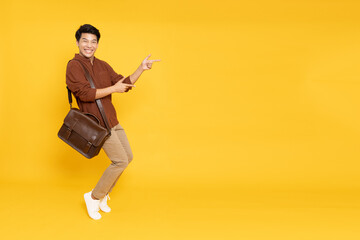 Portrait of happy excited Asian man office worker pointing hands to empty space on isolated yellow...