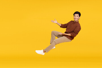 Happy cheerful young Asian man floating in the air isolated on yellow background, Presentation...