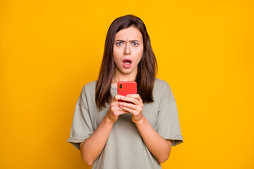 Photo of upset shocked young woman hold phone negative comment reaction isolated on yellow color...