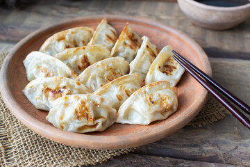 Gyoza with sesame seeds and micro greens in a ceramic dish with soy sauce and bamboo sticks on a wooden table. Rustic style. Traditional Asian food concept. Horisontal orientation. Close-up.