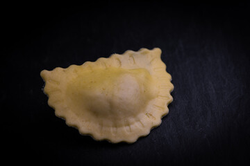Tasty raw ravioli with flour and spinach on dark background, process of making italian ravioli