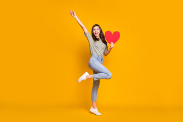 Fototapeta na wymiar Full length body size view of pretty cheerful girl holding in hands heart jumping having fun isolated over bright yellow color background