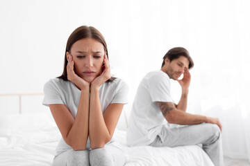 Sad unhappy upset resentful european young wife ignores husband after quarrel, sitting in bed