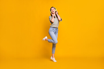 Fototapeta na wymiar Full length body size view of lovely cheerful girl jumping listening melody isolated over bright yellow color background