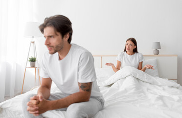 Fototapeta premium Upset offended young european man sitting on bed ignoring lady. Wife shouting and quarreling in bedroom