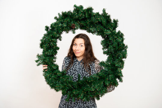 Smiling young woman looking through a green Advent Christmas wreath on a white background