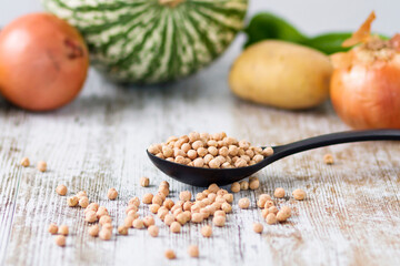A kitchen spoon with raw chickpeas and other vegetables in the background
