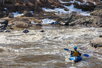 man in a kayak on the water among the stormy river and stones. dangerous descent along the river